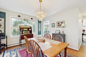 A dining room with a wooden table, chairs, a chandelier, and a rug. - Private spacious mountain view w/ beach rights, hot tub, spacious deck & firepit (Ossipee)