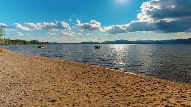Una playa con cielo despejado, agua tranquila y montañas a lo lejos.