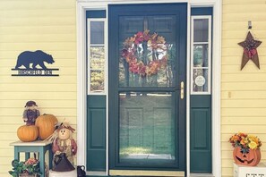 A front door with a wreath, a bear logo, a star decoration, and Halloween pumpkins. - Private spacious mountain view w/ beach rights, hot tub, spacious deck & firepit (Ossipee)