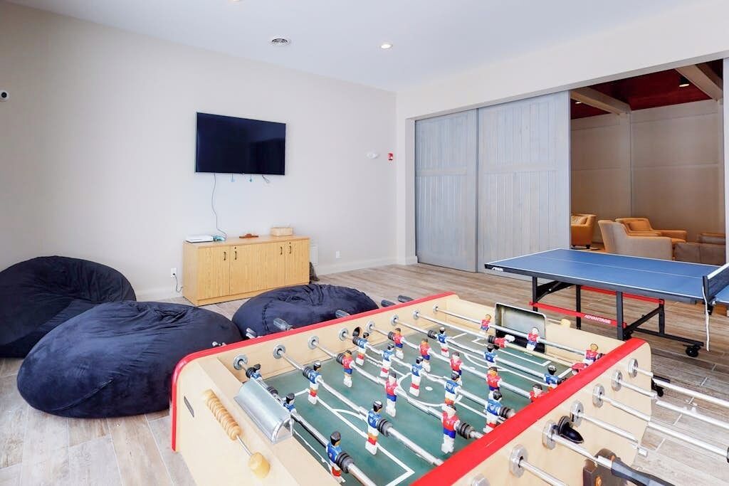 Una habitación con mesa de futbolín, pufs, televisor y puerta corredera que da a otra zona.