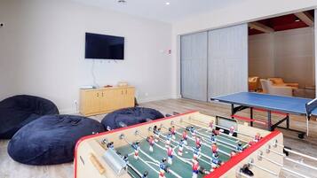 Una habitación con mesa de futbolín, pufs, televisor y puerta corredera que da a otra zona.
