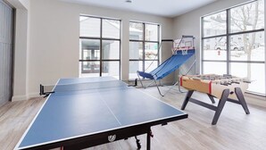 Une pièce équipée d’une table de ping-pong, d’un baby-foot, d’un fauteuil bleu et de grandes fenêtres.