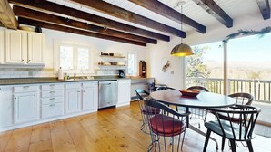 Una cocina con armarios blancos, suelo de madera y un comedor con mesa y sillas redondas.