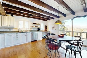 A kitchen with white cabinets, a wooden floor, and a dining area with a round table and chairs. - Mtn-view home with large deck, wood stove, firepit, grill, streaming, W/D, & AC (Thornton)