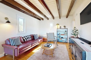 A living room with a leather sofa, a striped chair, a coffee table, and a bookshelf. - Mtn-view home with large deck, wood stove, firepit, grill, streaming, W/D, & AC (Thornton)