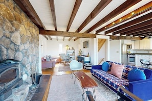 A cozy living room with a stone fireplace, a blue sofa, and a wooden ceiling. - Mtn-view home with large deck, wood stove, firepit, grill, streaming, W/D, & AC (Thornton)