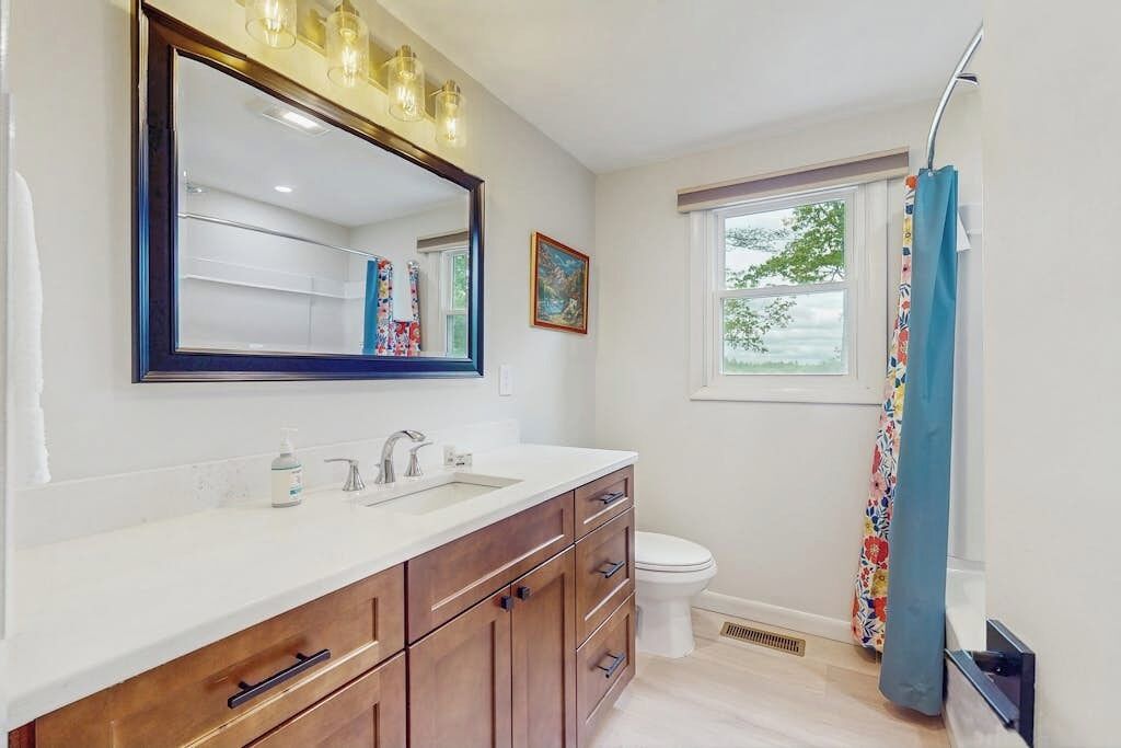 Un baño con un espejo grande, un lavabo, un inodoro y una ventana con vistas.