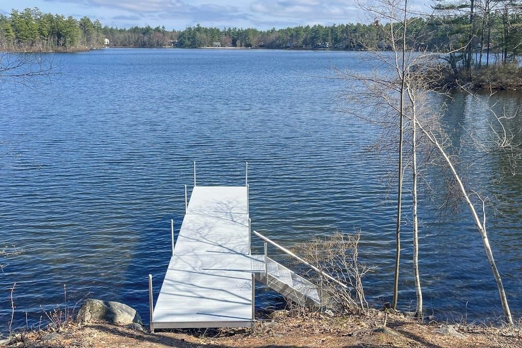Um cais se estende por um lago calmo, com uma margem coberta por vegetação.