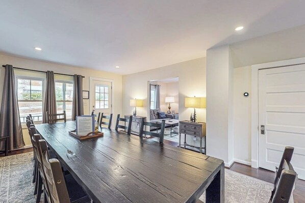 A spacious dining area with a long table, chairs, and a small seating area with a sofa and lamp.