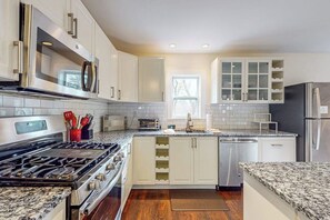 A modern kitchen with stainless steel appliances, white cabinetry, and a granite countertop.