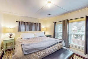 A hotel room with a large bed, bedside lamps, a bench, and a window with curtains.