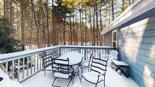 Une terrasse extérieure couverte, avec une table et des chaises, entourée d’une rambarde et d’un sol recouvert de neige.