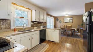 Une cuisine avec des meubles blancs, un plan de travail en granit, un réfrigérateur noir et un coin repas avec des chaises en bois.