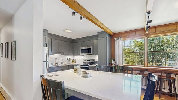 A modern kitchen with a large island, grey cabinets, and a view through large windows. - Intown home w/ views, private deck & firepit; close to  Mt. Cranmore (North Conway)