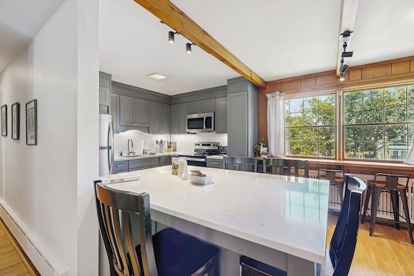 A modern kitchen with a large island, grey cabinets, and a view through large windows. - Intown home w/ views, private deck & firepit; close to Mt. Cranmore (North Conway)
