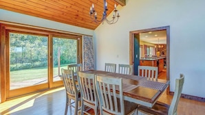 A dining area with a wooden table and chairs, large windows, and a view of the outdoors.
