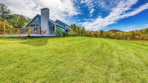 A modern house with a large lawn, a wooden deck, and a mountain in the background.