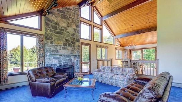 A spacious living room with a stone fireplace, leather sofas, and large windows offering views of the outdoors.