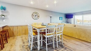 Un comedor con una mesa y sillas de madera, un reloj en la pared y un sofá al fondo.