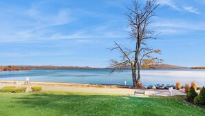 Vista del lago con zona verde, un banco y un árbol.