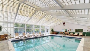 An indoor swimming pool with a glass ceiling, lounge chairs, and a view of trees outside. - Mountainside condo w/ pool & rec room; walk to lifts & town (Lincoln)