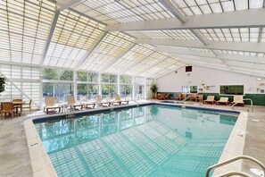 Ein Hallenbad mit Glasdach, Liegestühlen und Blick auf Bäume.