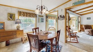 Un comedor con una mesa de madera, sillas, una araña y vistas al exterior.