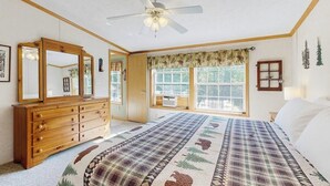 Un dormitorio con una cama grande, un aparador de madera, un ventilador de techo y una ventana con cortinas.