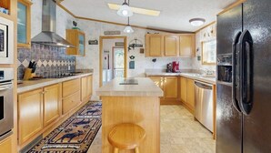 Una cocina con armarios de madera, una isla central con un taburete, un refrigerador negro y un ventilador de techo.
