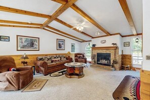 Ein geräumiges Wohnzimmer mit Kamin, Holzbalken, einem runden Couchtisch und einer Couch.