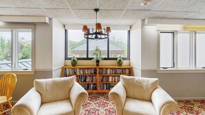 Ein Zimmer mit einem großen Fenster, einer Bücherwand, zwei Sesseln und einer Kristallleuchter.