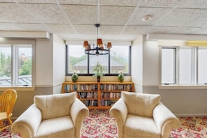 Ein Zimmer mit einem großen Fenster, einer Bücherwand, zwei Sesseln und einer Kristallleuchter.
