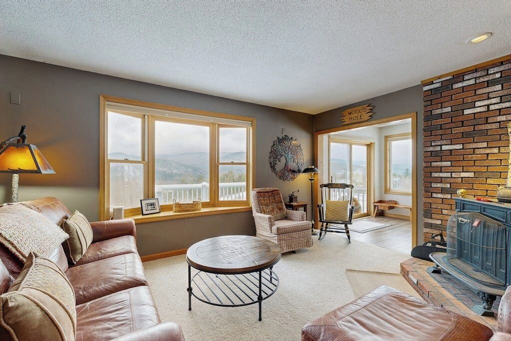 A living room with a fireplace, leather sofa, round coffee table, and large windows.