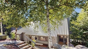 Moderni talo, jossa on metallikatto, portaat, jotka johtavat sisäänkäynnille, ja taloa ympäröivä metsäalue.