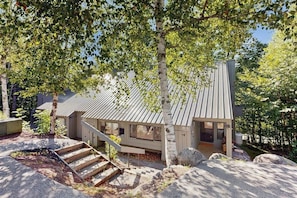 Ein modernes Haus mit Metalldach, einer Treppe zum Eingang und einer umliegenden bewaldeten Gegend.