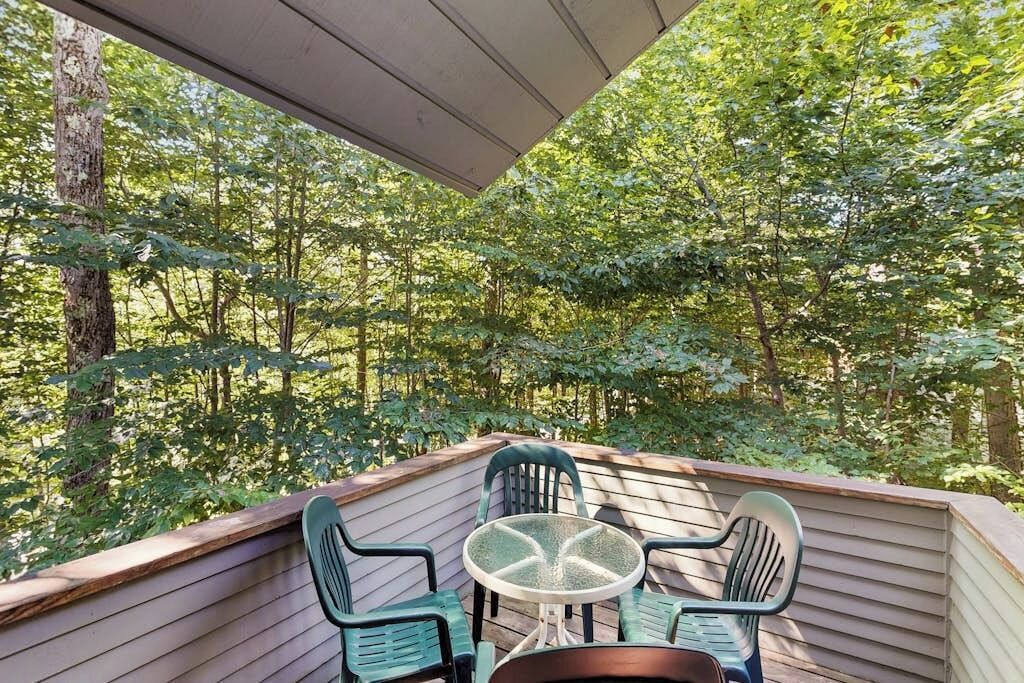 Une terrasse extérieure couverte, dotée d’une table et de chaises, et entourée d’arbres denses.