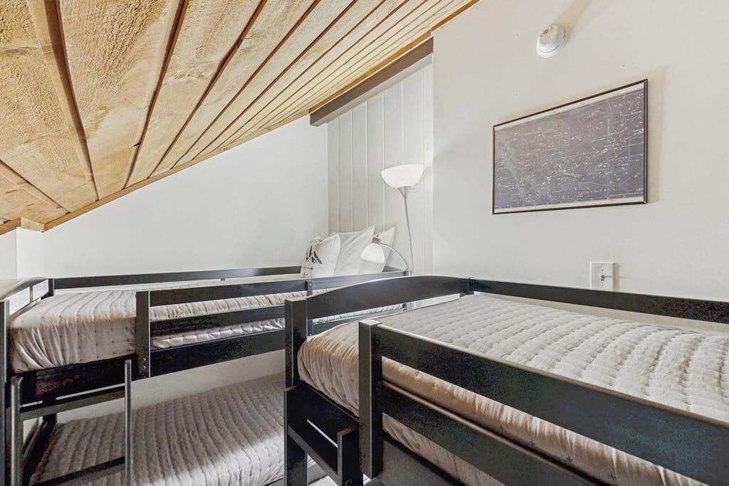 A dormitory room with bunk beds, a desk, a chair, a lamp, and a framed picture on the wall.