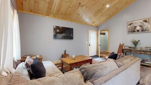 A cozy living room with a wooden ceiling, a television, a sofa, a coffee table, and a door leading to another room.