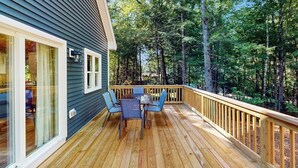 A deck with a table and chairs, surrounded by a wooden railing, overlooking a forested area.
