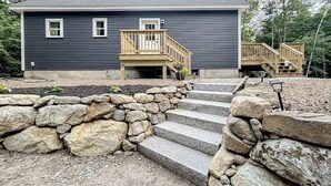 A two-story house with a stone staircase leading to a wooden deck.