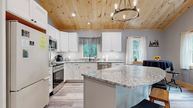 A kitchen with a granite island, white cabinets, a wooden ceiling, and a chandelier.
