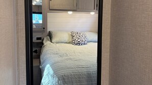 Quarto com cama, almofadas, mesa de cabeceira, cômoda e janela.