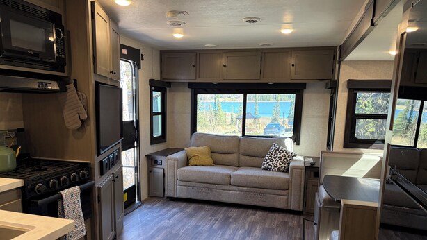 Cozinha compacta de motorhome com fogão, micro-ondas e sofá com vista.