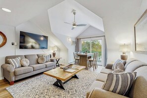Ein geräumiger Wohnbereich mit hoher Decke, Deckenventilator, großem Fenster, Esstisch und einer Couch.