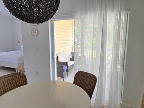 A room with a bed, a table, wicker chairs, a hanging light fixture, and a view through a glass door to an outdoor seating area. - Costa Azul Bimini Bay (Bailey Town)