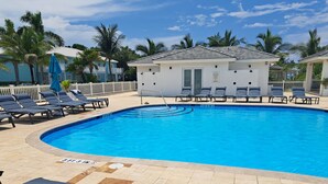 Ein Swimmingpool mit Liegestühlen, ein kleines Gebäude und Palmen.