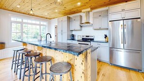 Une cuisine moderne avec un plafond en bois, des appareils en acier inoxydable et un coin bar avec des tabourets.
