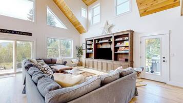 Un salon spacieux avec un grand canapé d’angle, des poutres apparentes en bois au plafond, un téléviseur et une bibliothèque.