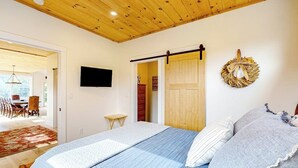 Une chambre à coucher comprenant un lit, un téléviseur, un plafond en bois, une porte et un élément décoratif mural.