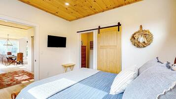 Une chambre à coucher comprenant un lit, un téléviseur, un plafond en bois, une porte et un élément décoratif mural.